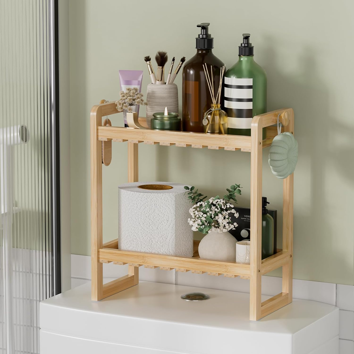 Two-tier bamboo bathroom shelf above a toilet holding bottles, a candle, and a plant.
