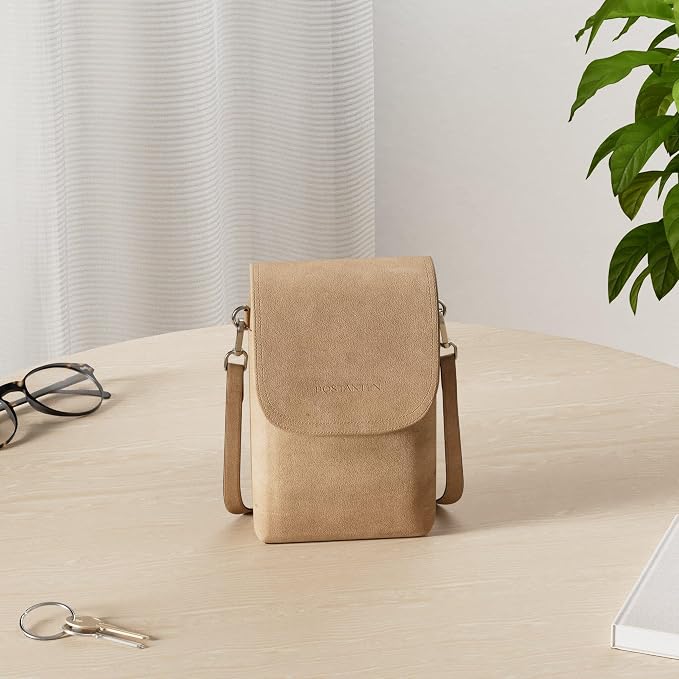 Small tan suede crossbody phone bag with a flap closure sitting on a wooden table.