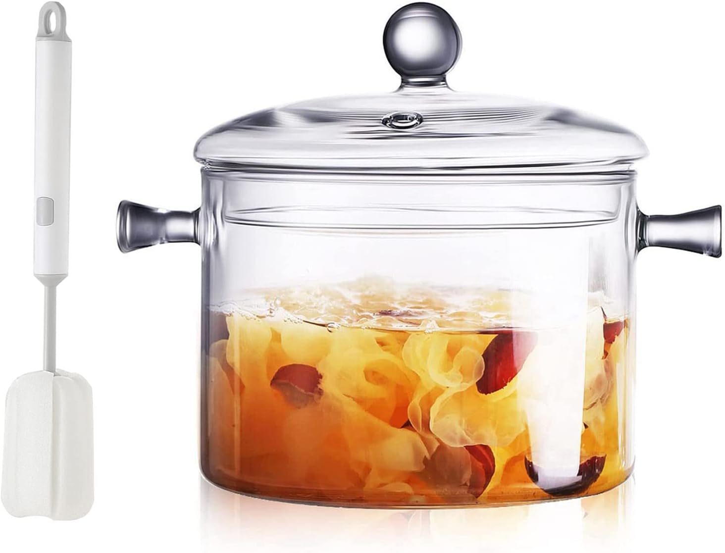 Clear glass stovetop saucepan with a lid, simmering fruit and spices inside, next to a silicone spatula.